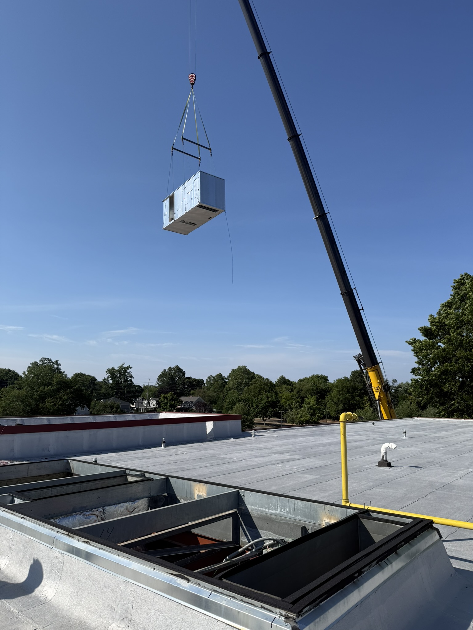 Crane lifting HVAC equipment above roof curbs