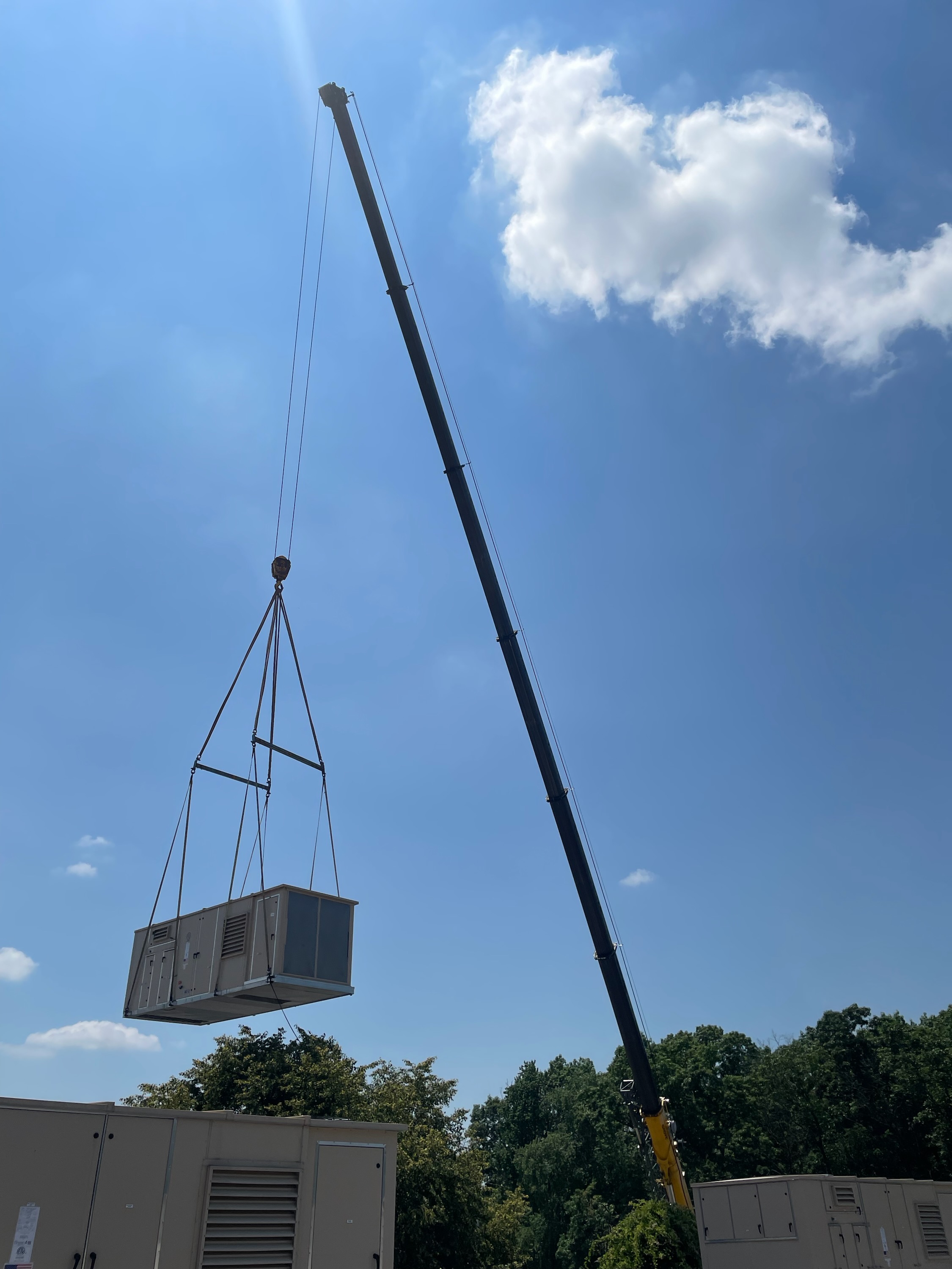 Crane hoisting an air handling unit above a rooftop